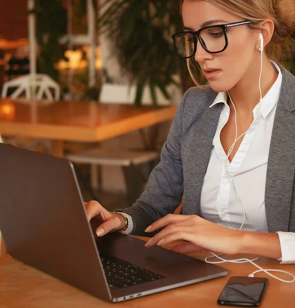 Egy üzletasszony laptopot használ a kávézóban. Egy fiatal, gyönyörű lány ül egy kávézóban, és számítógépen dolgozik. Életmód és üzleti koncepció. — Stock Fotó
