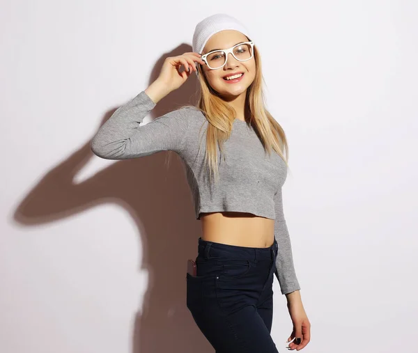 Életmód és emberek koncepció: fiatal aranyos mosolygós hipster lány fehér szemüveget és kalapot visel. — Stock Fotó