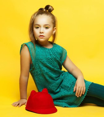 Sarı arka planda poz veren sarı saçlı küçük moda kızı.