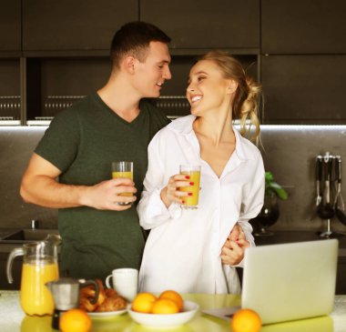 Genç çift mutfakta kahve içip dizüstü bilgisayarda çalışıyor.