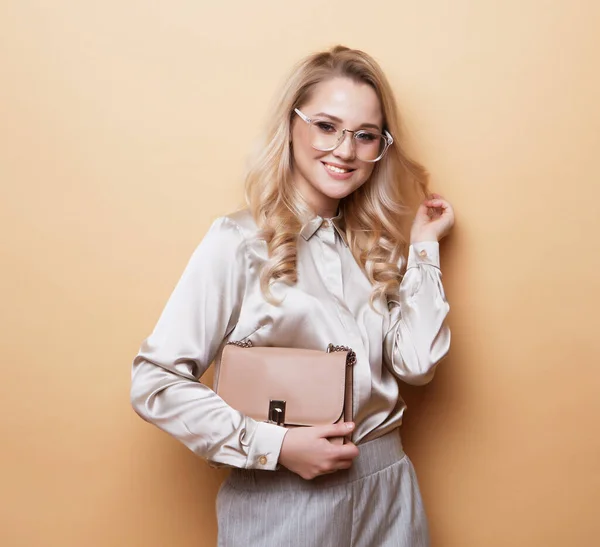 Красивая блондинка в блузке и брюках в очках, держащая сумочку. — стоковое фото