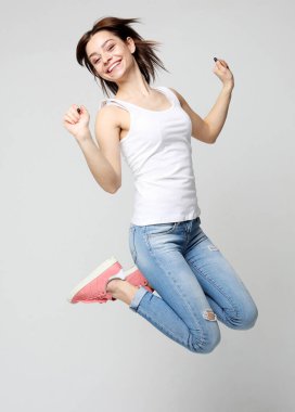 Gülümseyen genç bir kadın beyaz arka planda havada zıplıyor