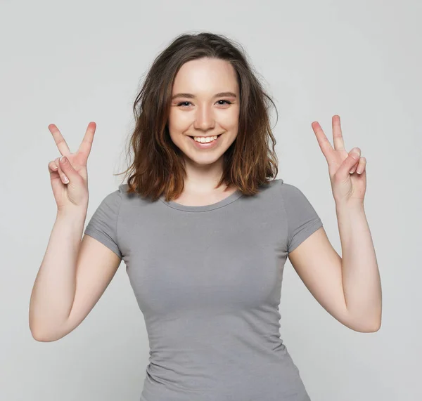 Šťastná dívka dívá na fotoaparát s úsměvem a ukazující mír znamení s prsty — Stock fotografie