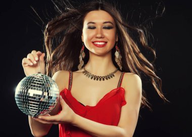 Kırmızı elbiseli genç esmer kadın siyah arka planda disko topu tutuyor.