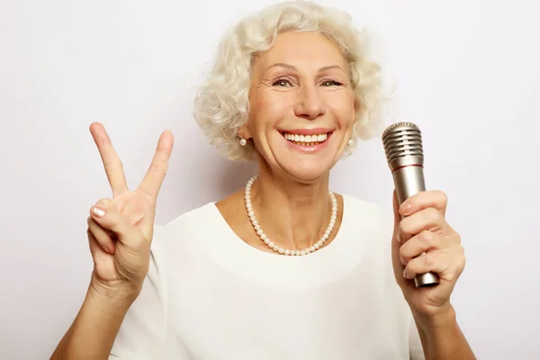 Retrato de la encantadora abuela moderna sostiene el soporte del micrófono y canta — Foto de Stock