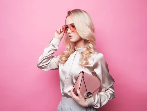 Mulher loira jovem bonita em uma blusa usando óculos, segurando bolsa . — Fotografia de Stock