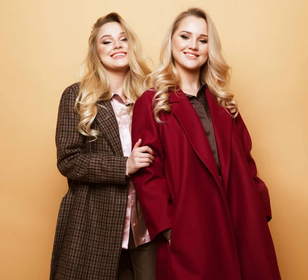 Fashion portrait of two girls, best friends posing indoor on beige background wearing winter stylish coat. — Stock Photo, Image