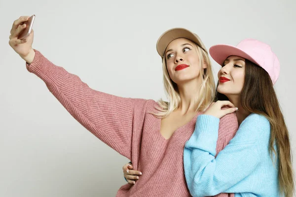 Duas adolescentes amigas em roupa hipster fazer selfie no telefone inteligente . — Fotografia de Stock