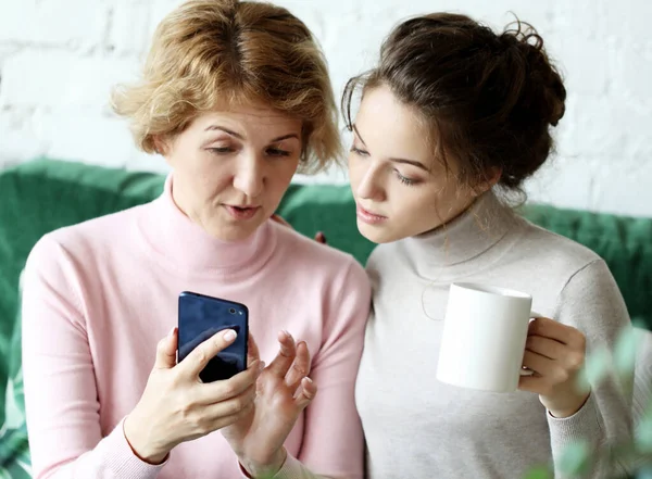 Οικογένεια και τεχνολογία. Ηλικιωμένη γυναίκα και η ενήλικη κόρη της χρησιμοποιούν smartphone στο σπίτι. — Φωτογραφία Αρχείου