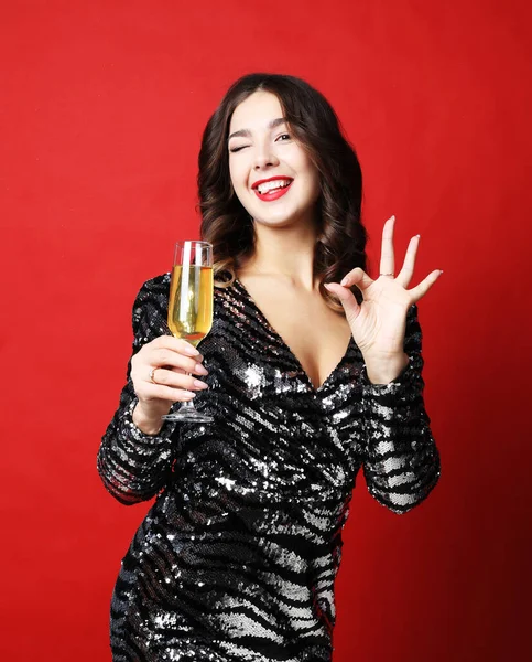 Siyah elbiseli kadın kırmızı arka planda bir kadeh şampanya tutuyor. — Stok fotoğraf