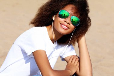 Güneş gözlüklü, kulaklıklı, cep telefonuyla müzik dinleyen büyüleyici afro-amerikalı genç kadın. Sıradan giyin..