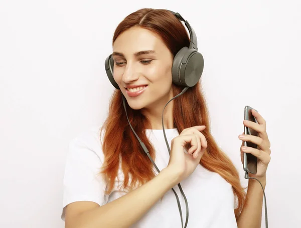 Hermosa joven en auriculares escuchando música sobre fondo blanco —  Fotos de Stock