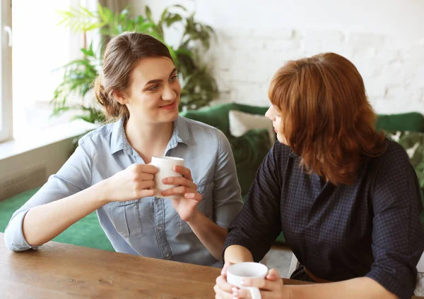 Beautiful mature mother and her adult daughter are drinking coffee — Stock Photo, Image