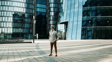 Takım elbiseli mutlu genç bir adam bir yaz günü modern bir iş merkezinin yakınında poz veriyor.