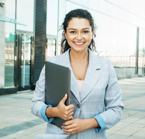 Genç Afrikalı Amerikalı kadın dışarıda, iş merkezinin yanında dizüstü bilgisayar kullanıyor.