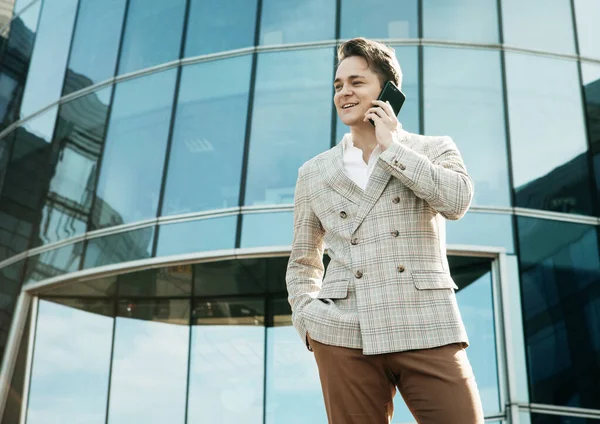 Young businessman dressed in formal clothes standing outside a glass building and using mobile — Stock Photo, Image