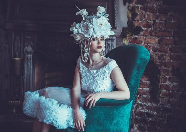 Güzel, genç, esmer bir gelin beyaz bir elbise giyiyor ve bir sandalyede çiçek çelengi oturuyor..