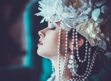 Güzel, genç, esmer bir gelin beyaz bir elbise giyiyor ve bir sandalyede çiçek çelengi oturuyor..