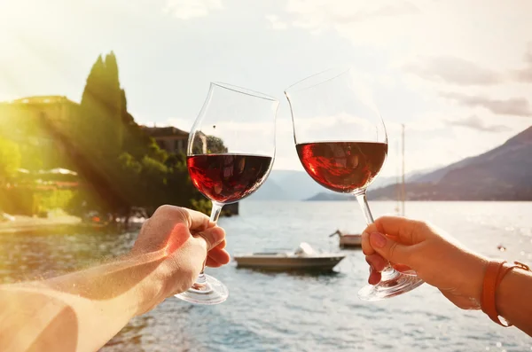 Wineglasses in hands against lake — Stock Photo, Image
