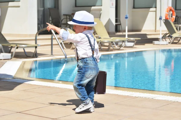male baby traveler with small suitcase near swimming pool