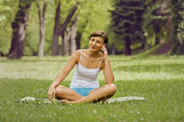 Mujer escuchando música en el prado, sonriendo . — Foto de Stock