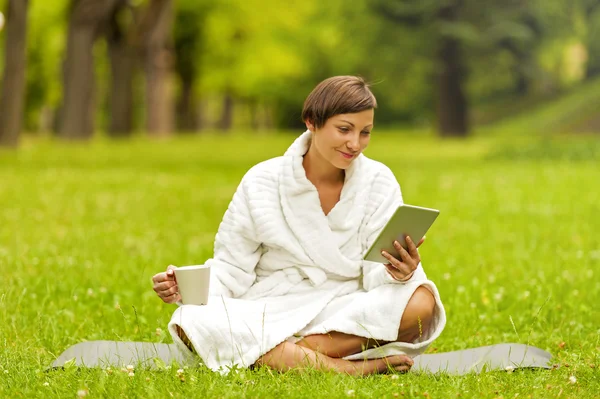 Bathrob yeşil çimenlerin üzerinde siting tablet, kullanan rahat kadın — Stok fotoğraf