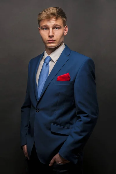 Joven hombre guapo en traje azul sonriendo sobre fondo oscuro —  Fotos de Stock