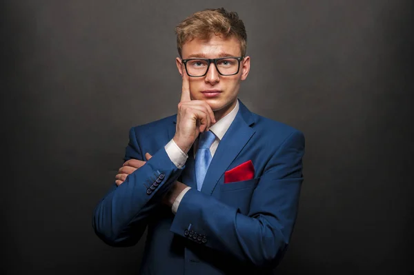 Junger gutaussehender Mann im blauen Anzug mit Brille, der auf dunklem Bac lächelt — Stockfoto