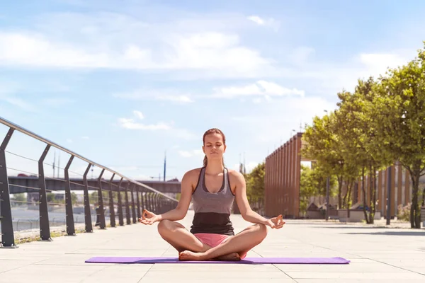 Genç kadının Yoga lotus pozisyonu nehrin yanında şehirde yapması, — Stok fotoğraf