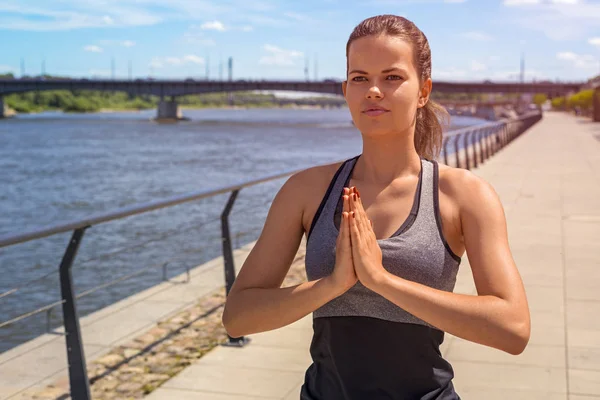 Young woman meditating in city by the river in summer, hands tog — Stock Photo, Image