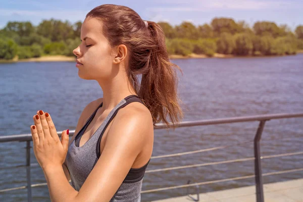 Young woman meditating in city by the river in summer, closed ey — Stock Photo, Image