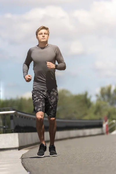 Young jogging man in the city in sportswear in gray color runnin