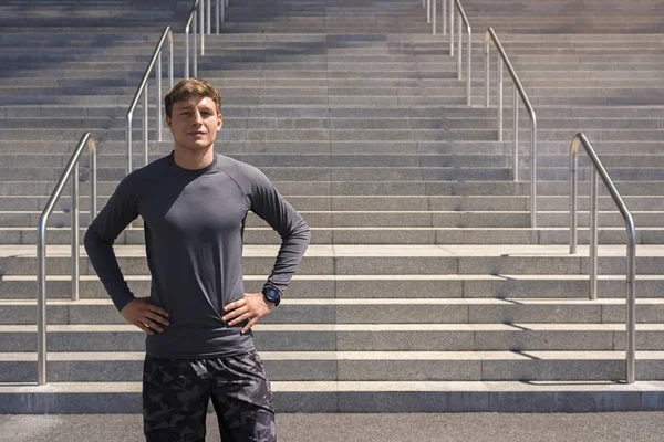 Nuori mies urheiluvaatteet kaupunkiympäristössä seisoo lepää jälkeen ex — kuvapankkivalokuva