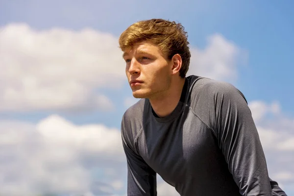 Young man resting after excercise on sunny day over sky with clo — Stock Photo, Image