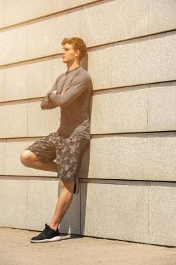 Kas yapı genç atlet geçti silah, yorgun açık havada, atletik jogger parlak spor giyim güzel beton duvar arka planda, fitness kavramı çalıştırdıktan sonra dinlenme içinde eğitim sonra