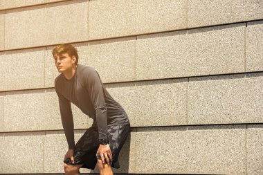 Erkek koşucu sabah sonra dinlenme çalıştırmak ile kopyalama alanı alanı metin mesajınız için duvar arka plan karşı dururken veya reklam, genç erkekler arasında eğitim açık havada mola yerleştirmek