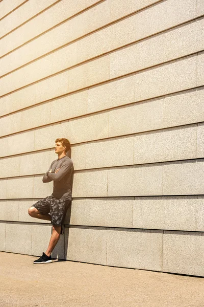 Male jogger resting after morning run while standing against wall background with copy space area for your text message or advertising, young fit men taking break between training outdoors