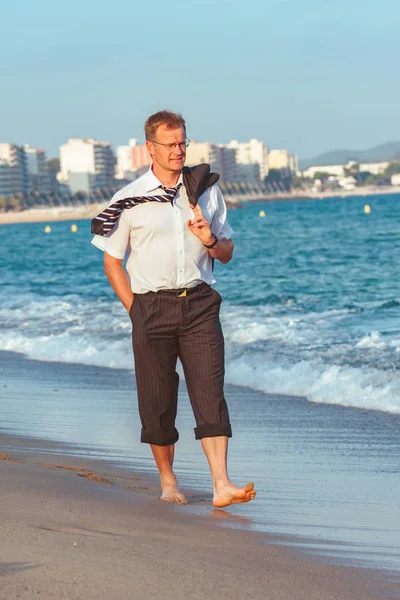 Молодой бизнесмен прогуливается по пляжу после рабочего времени — стоковое фото