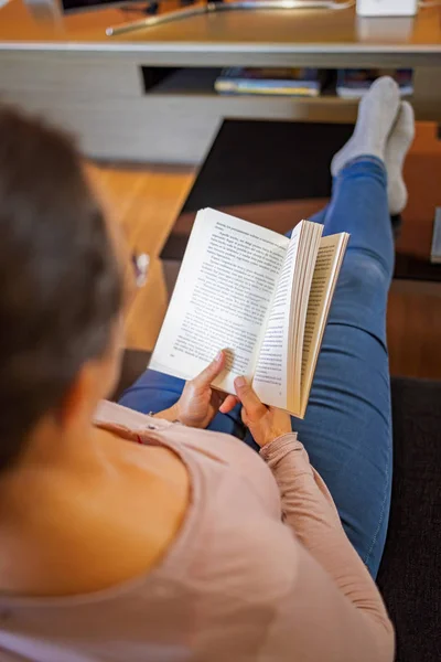 Pretty spanish women reading at home on the sofa — Stock Fotó