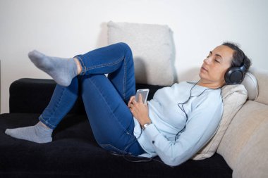 Young Spanish woman listening to music at home with headphones