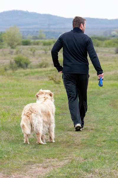 Jovem correndo com seu cão golden retriever no prado — Fotografia de Stock