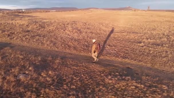 写真家は日没の光の中で牧草地を歩く 空中ドローン映像 — ストック動画