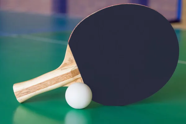 黑色木制球拍的 ping pong 和白球躺在绿色的桌子上. — 图库照片