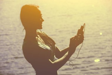 Eşofman bir smartphone cep telefonu ile müzik dinlemek içinde genç bir kadın atlet silüeti