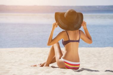 Attractive, young girl in a bathing suit sitting on the beach clipart