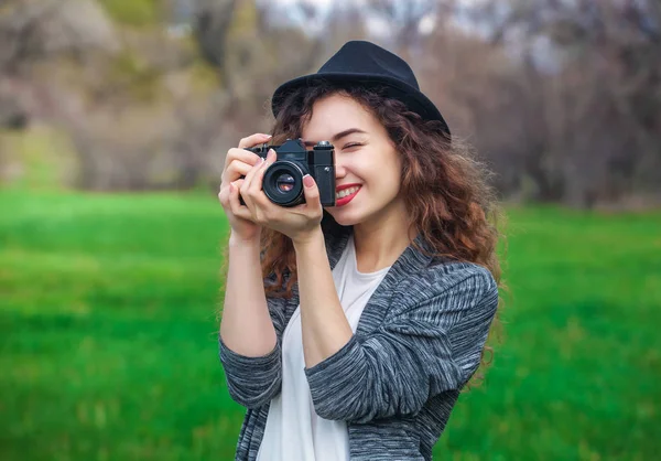 Menina-fotógrafo bonita com cabelo encaracolado segurando uma câmera velha e tirar uma foto — Fotografia de Stock