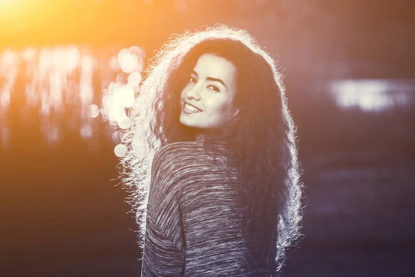 Χαμογελαστός, όμορφο κορίτσι με σγουρά, μαλλιά φωτίζονται από τον ήλιο — Φωτογραφία Αρχείου