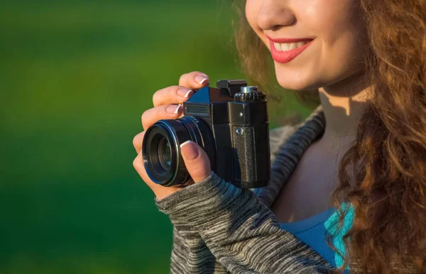 Menina-fotógrafo bonita com cabelo encaracolado segurando uma câmera velha e tirar uma foto, na primavera ao ar livre no parque . — Fotografia de Stock