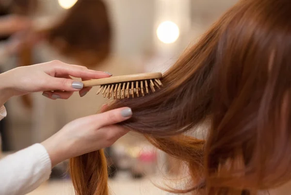 Peluquería peinando su pelo largo y rojo de su cliente en el salón de belleza . — Foto de Stock