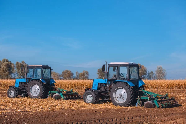 Zwei große blaue Traktoren pflügen ein Feld um und entfernen die Überreste des zuvor gemähten Mais. die Arbeit der Landmaschinen. — Stockfoto